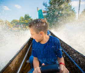 Een jongen in een boomstam in de wildwaterbaan Ripsaw Falls in Slagharen wordt nat van de opspattende golven.