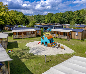 Moderne lodges en chalets gegroepeerd rondom een klein speelveld op de camping