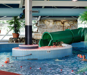 Kinderen hebben plezier bij de grote groene waterglijbaan in het overdekte zwembad van Vakantiepark Weerterbergen in Limburg.