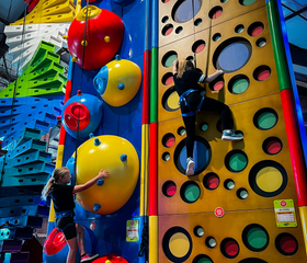 Kinderen met klimgordels klimmen op een kleurrijke en uitdagende indoor klimwand (Clip 'n Climb) bij Vakantiepark Westerbergen.