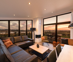 Stijlvolle woonkamer in een vakantiehuis op Vakantiepark Zeedijk met een grote hoekbank en een prachtig uitzicht over de polder tijdens zonsondergang.