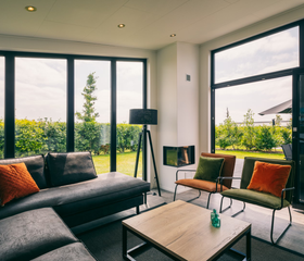 Gezellige zithoek met een comfortabele bank en een moderne haard in een vakantiehuis op Vakantiepark Zeedijk, met uitzicht op de groene omgeving.