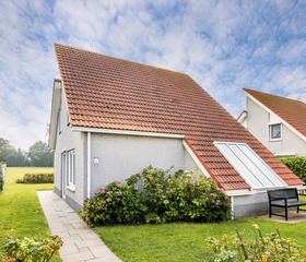Buitenkant van een vrijstaande vakantievilla met een puntdak en een grote tuin op Vakantiepark Zeeland Village.