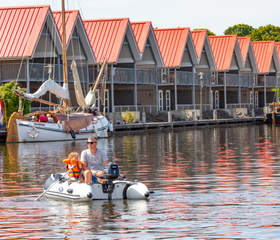 Een gezin met kinderen vaart in een rubberboot langs de waterwoningen van Waterpark Terherne op een zonnige dag.