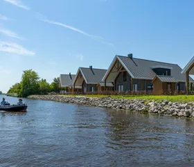 Een bootje met mensen vaart op een zonnige dag langs de moderne waterlodges van Waterpark Zwartkruis.