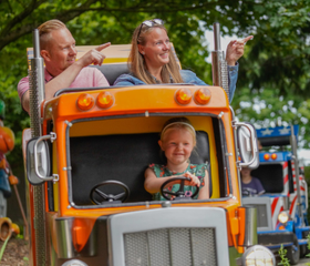 Lachend meisje achter het stuur van een oranje speelgoedtruck in een kinderattractie in Wunderland Kalkar.