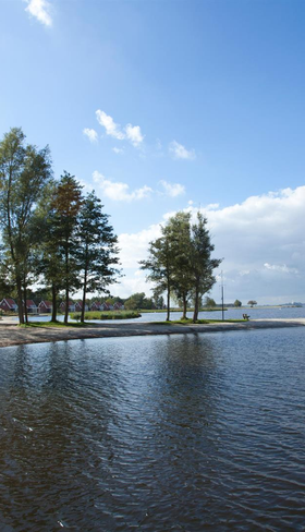 Uitzicht over het kabbelende Veluwemeer vanaf het zandstrand van Vakantiepark Bad Hoophuizen op een zonnige dag.
