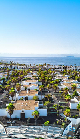 Luchtfoto van de witte bungalows en het zwembad van Relaxia Lanzasur Club op Lanzarote, met de oceaan op de achtergrond.