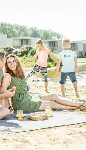 Gezin met kinderen geniet van een zonnige dag met een picknick op het zandstrand bij het water op Camping de Schatberg.