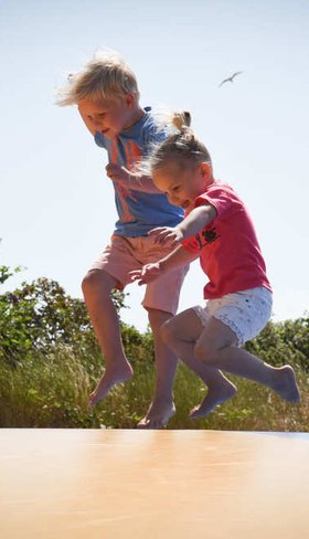 Twee kinderen springen hoog in de lucht op de airtrampoline in de duinen van Camping Loodsmansduin.