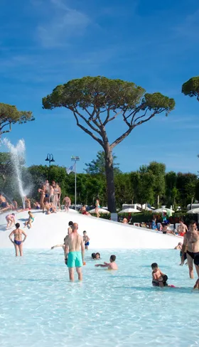 Gasten zwemmen in het kindvriendelijke lagune zwembad met zachte bodem en fonteinen, omringd door pijnbomen op camping Park Albatros in Toscane.