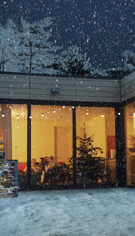 Een sfeervol verlichte cottage in een besneeuwd landschap bij Center Parcs De Kempervennen tijdens Winter Wonderland, met een kerstboom voor het raam.