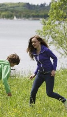 Kinderen spelen en rennen vrolijk in het gras aan de oever van het grote Bostalmeer bij Center Parcs.