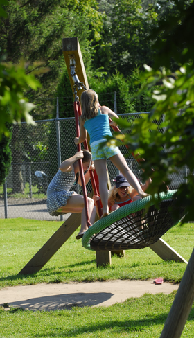 Drie kinderen hebben plezier op een grote nestschommel in de buitenspeeltuin van Recreatiepark De Scherpenhof in Gelderland.