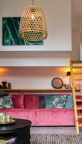 Een hippe en kleurrijk ingerichte woonkamer in een vakantiehuis op Droompark De Zanding, met een roze bank en een houten ladder naar de vide.
