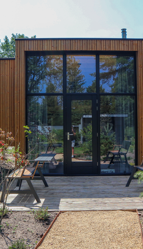 Een moderne, houten vakantiewoning met een grote glazen pui en een terras met een picknicktafel op Droompark Hooge Veluwe.