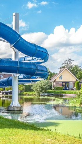 Blauwe waterglijbaan naast een gebouw aan een vijver met vakantiehuisjes bij BungalowSpecials