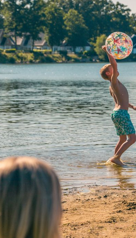 Kind speelt met een bal in het water van de recreatieplas op EuroParcs Resort Limburg, met een zandstrand op de voorgrond.