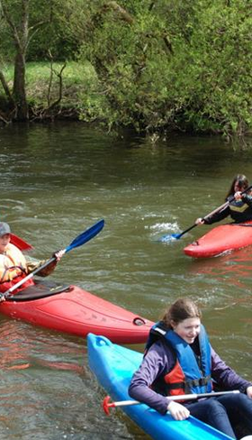 Een groep kinderen en volwassenen is aan het kajakken en kanoën op een rivier in de Eifel tijdens hun verblijf in Feriendorf Felsenhof.