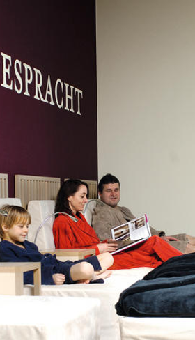 Een gezin relaxt samen op een comfortabele bank in de 'Mondesperacht' lounge van Ferienresort Bad Bentheim.