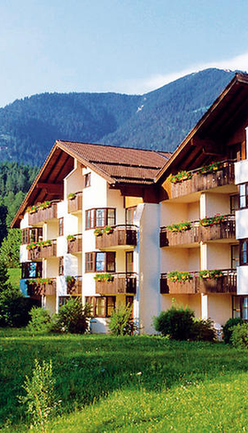 De buitenkant van het Dorint Sporthotel in Garmisch-Partenkirchen, omgeven door groene gazons en met de Beierse Alpen op de achtergrond.