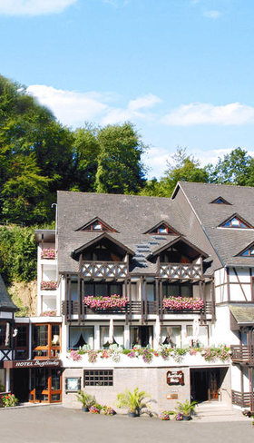 Hotel Burgfrieden, een charmant gebouw in traditionele stijl, gelegen tegen een groene heuvel met een indrukwekkende kasteelruïne op de achtergrond, in de Moezelstreek.