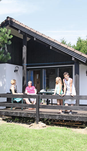 Een gezin ontspant op de houten veranda van hun vakantiehuis in Eifelpark Kronenburger See in de Duitse Eifel.
