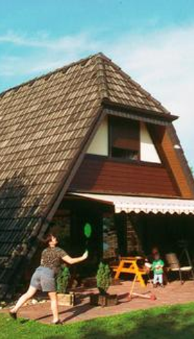 Een A-frame vakantiehuisje op Feriendorf Waldbrunn in het Zwarte Woud, met een familie die ontspant en badmintont op het terras.