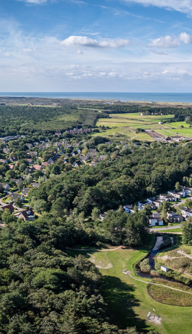 Luchtfoto van Kustpark Texel en de bosrijke omgeving van De Koog, met de Noordzee aan de horizon.