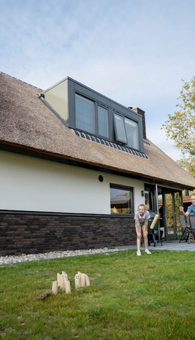 Een familie ontspant op het terras van een moderne, rietgedekte duinvilla met grote tuin op vakantiepark Landal Berger Duinen.