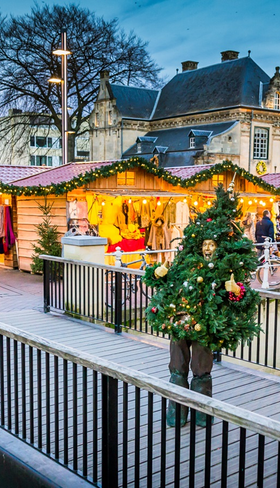 De sfeervolle kerstmarkt in het centrum van Valkenburg, met verlichte kraampjes, een kerstboom en bezoekers op een brug.