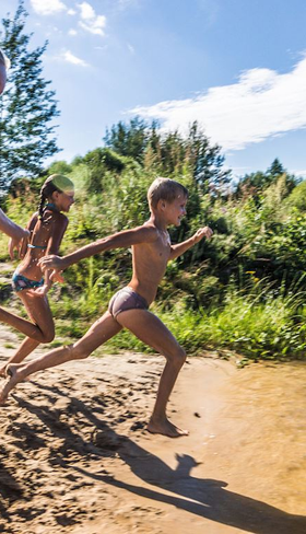 Een groep kinderen rent lachend vanaf een zandstrandje een recreatiemeer in op vakantiepark Landal Drentse Lagune in Drenthe.
