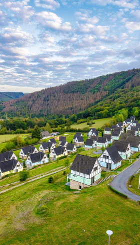 Luchtfoto van vakantiepark Landal Eifeler Tor in de Eifel, met de vakwerkhuizen en appartementen gelegen in een groen dal aan het stuwmeer.