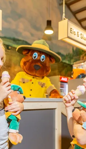 Twee kinderen eten een ijsje dat ze hebben gekregen van mascotte Bollo de Beer in het centrumgebouw van Landal Hochwald.