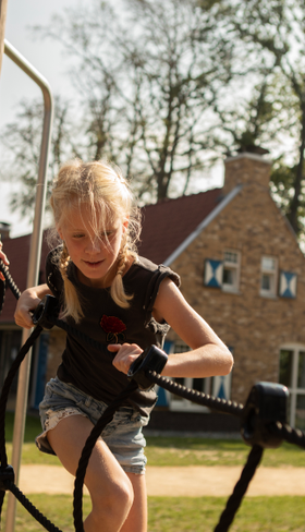 Twee meisjes klimmen en klauteren op een avontuurlijk touwenparcours in de speeltuin van Landal Kaatsheuvel.