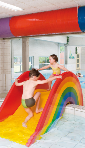 Kinderen spelen in het overdekte zwembad en glijden van een vrolijke regenboog kinderglijbaan bij Landal Natuurdorp Suyderoogh.