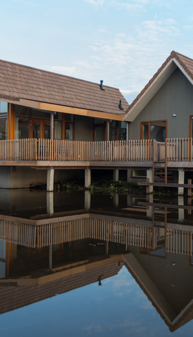 Een luxe, vrijstaande waterwoning op palen met een houten veranda, die prachtig reflecteert in het kalme water van de Reeuwijkse Plassen bij Landal.