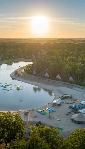 Luchtfoto van Landal 't Loo op de Veluwe met de grote recreatieplas, het strand en de omliggende bossen tijdens zonsondergang.
