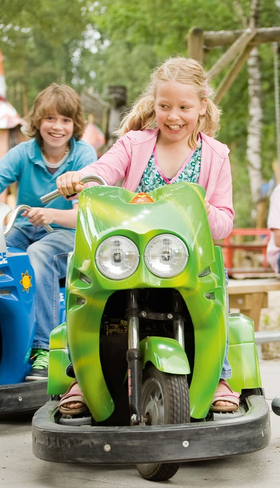 Kinderen rijden op een groene en blauwe scooter op het verkeersplein van Landal Twenhaarsveld, terwijl de ouders toekijken.