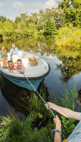 Een jongen trekt een sloep met zijn familie aan boord naar de waterkant in de groene, waterrijke omgeving van Landal Waterresort Blocksyl.