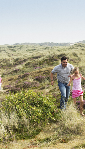 Gezin met kinderen rent en speelt in de duinen op Terschelling, vlakbij Landal West-Terschelling.