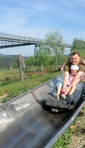 Een vader en dochter roetsjen van de zomerrodelbaan (Sommerrodelbahn) op de Erlebnisberg Kappe, een populaire attractie in de buurt van Landal Winterberg.