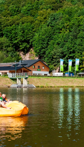 Een gezin heeft plezier op een gele waterfiets op het recreatiemeer van Landal Wirfttal, omringd door de groene heuvels van de Eifel.