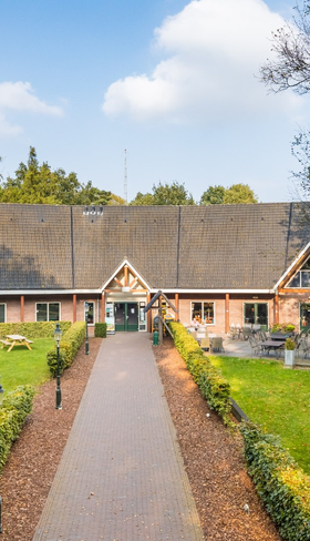 Het sfeervolle hoofdgebouw van vakantiepark Landgoed het Grote Zand in Drenthe, met op het grasveld een grote airtrampoline.