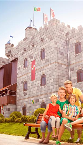 Een vrolijk gezin zittend op een bankje voor het indrukwekkende LEGO kasteelhotel (Königsburg) in het LEGOLAND Feriendorf in Beieren.