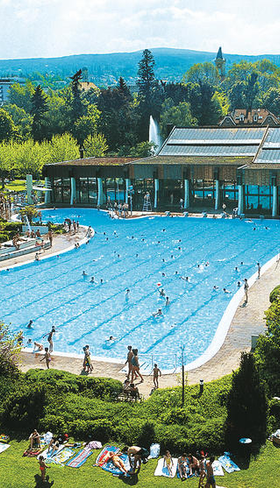 Overzicht van het grote openluchtzwembad Salinarium in Bad Dürkheim, direct naast het Mercure Hotel, met veel mensen die zwemmen en zonnebaden op een zonnige dag.