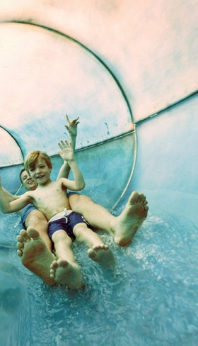 Een jongen glijdt met zijn armen in de lucht met hoge snelheid door een doorzichtige waterglijbaan in het zwemparadijs Aqua Mundo van Center Parcs Park Allgäu.