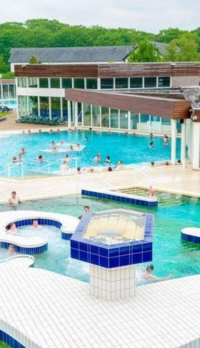 Overzicht van de thermaalbaden van Roompot Klein Vink in Limburg met zwemmende gasten in het water, omringd door natuur.