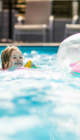 Jong meisje met zwemvleugels speelt met een opblaasbare bal in het blauwe water van het buitenzwembad op Recreatiepark Beekbergen.