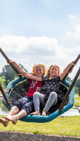 Twee meisjes hebben samen plezier op de grote vogelnestschommel in de speeltuin van Recreatiepark Het Esmeer.
